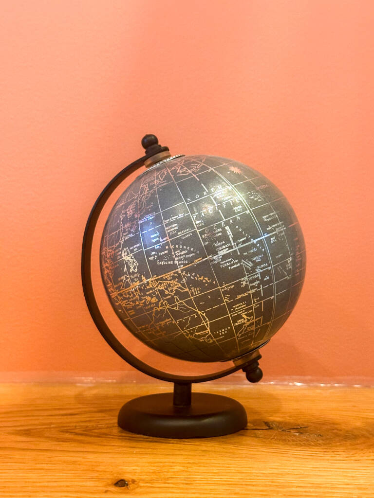 Petit globe terrestre gris avec armature noire sur un fond corail et un support en bois