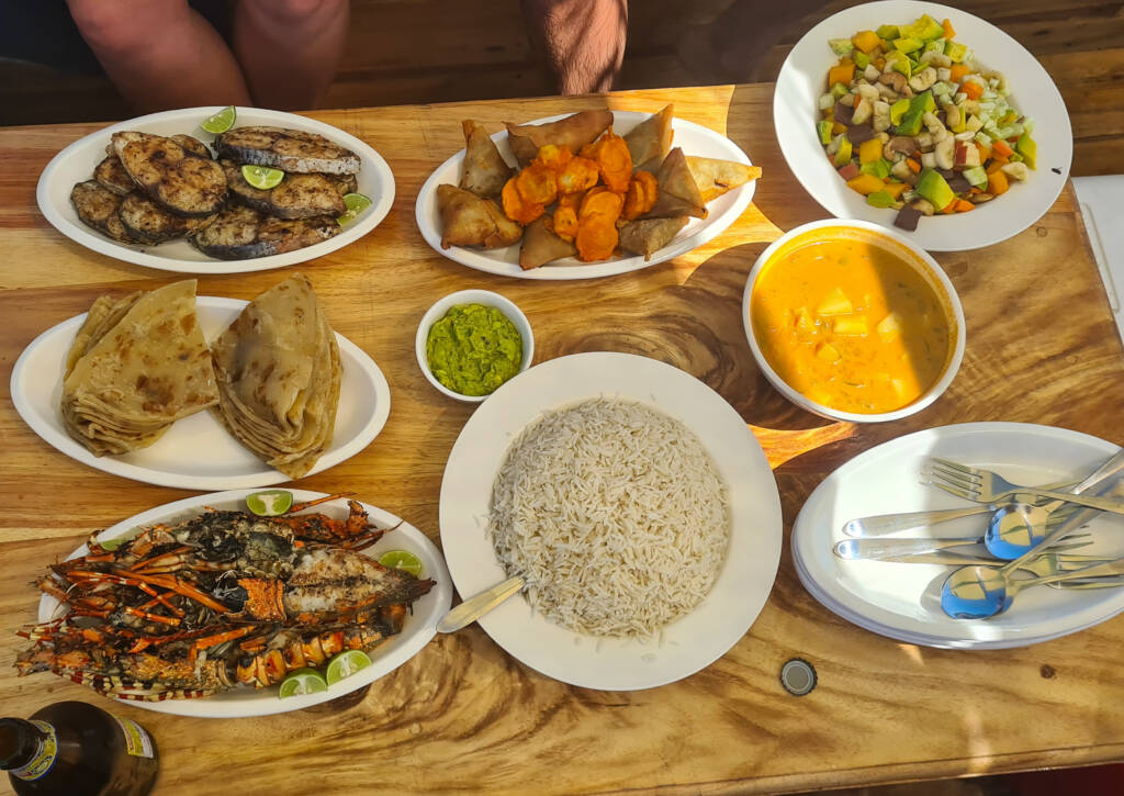 Repas composé de langouste, riz, légumes, samoussas...